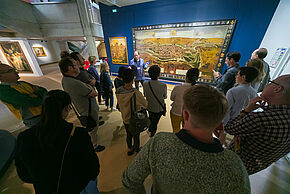 Des visiteurs du musée devant une oeuvre expliquée par une guide.