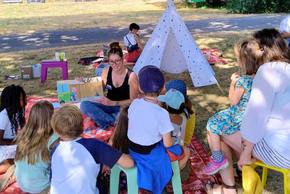 Une bibliothécaire lit des livres à des enfants sur une pelouse.