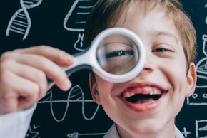 Un enfant avec une blouse blanche regarde à travers une loupe.
