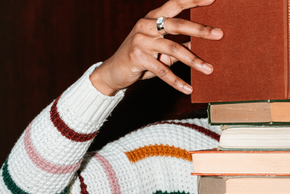 Une personne lit un livre posé sur une pile de livres.