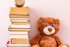 Une peluche est assise à côté d'une pile de livres sur laquelle est positionné un réveil.